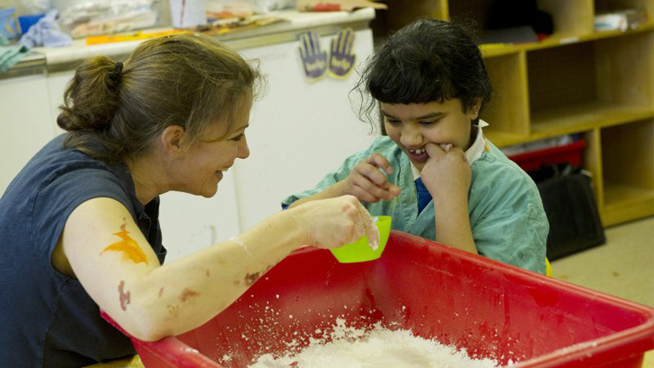 A girl smiles as her teacher
                  holds a plastic cup over a container of white powder