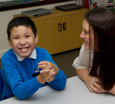 A boy and his teacher sit at a table,
                  smiling