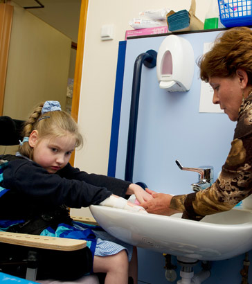 A teacher helps a girl to wash her
                  hands