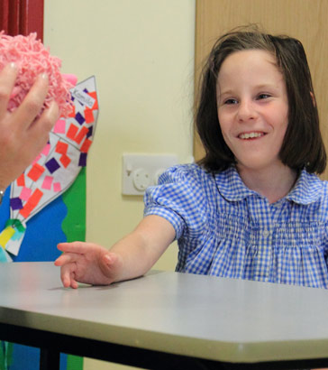 A girl smiles as a teaching sitting opposite
                  her holds up an object