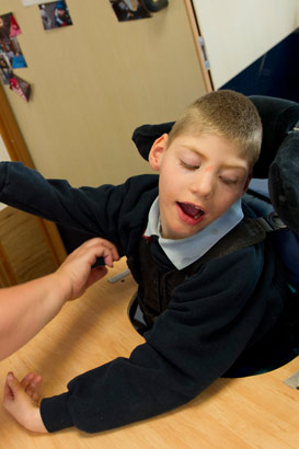 A boy in a specialist chair interacts
                  with a teacher