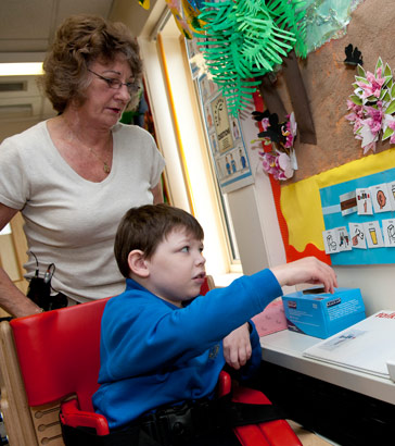 A boy, supervised by a teacher,
                  reaches towards a wall