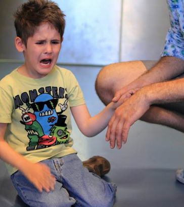 A distressed boys holds a male teacher's hand