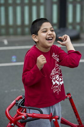 A boy with walking support laughs
                  in a playground
