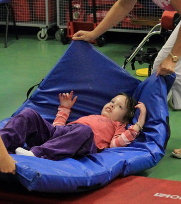 A child being lifted on a mat by two carers
