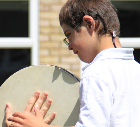 Teacher and boy enjoy playing with a tambourine
                  on a school's lawn