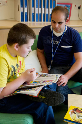 a child sits on a sofa reading
                  with his caregiver