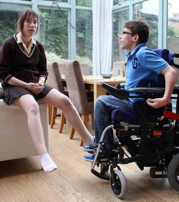 Brother in automated wheelchair talks to his
                  sister in the conservatory of their family home
