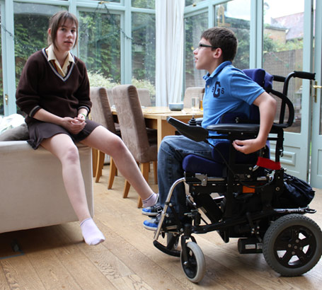 Brother in automated wheelchair talks to his
                  sister in the conservatory of their family home