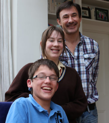 A father, daughter and son standing together
                  in front of a bookshelf in their house