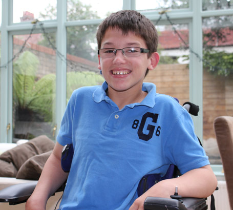 boy in blue shirt in automated wheelchair
                  smiles at the camera