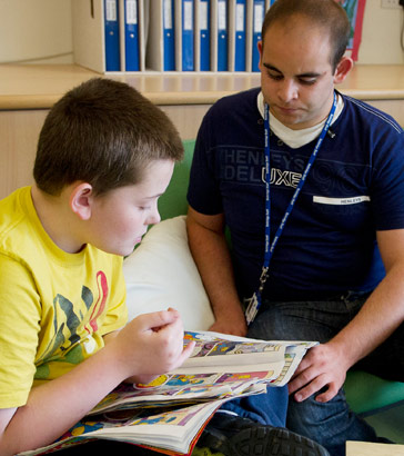 A teacher sits with a boy and
                  helps him to take part in one of his reading interests