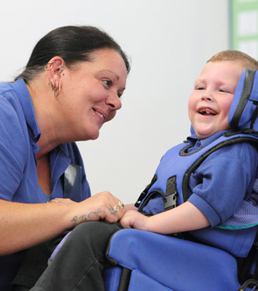teacher and boy in wheelchair smiling
                  at each other