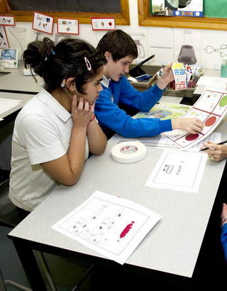 Three children and a teacher
                  attach stickers to a self-assessment form