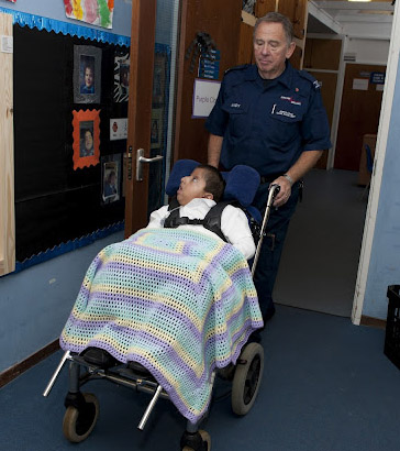 A boy, covered in a blanket, being
                  wheeled along a school corridor