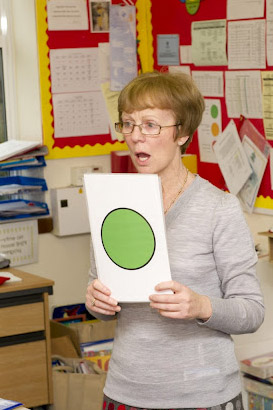 A teacher holding up a card depicting
                  a green disc