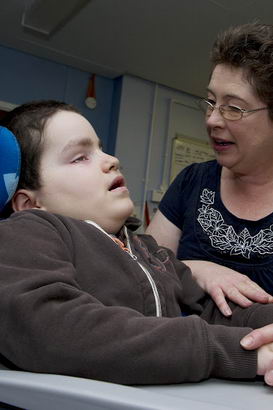 A carer holds the hand and arm
                  of a boy in a specialist chair