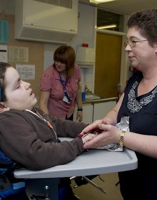 A carer holds some foil in the
                  hand of a boy in a specialist chair