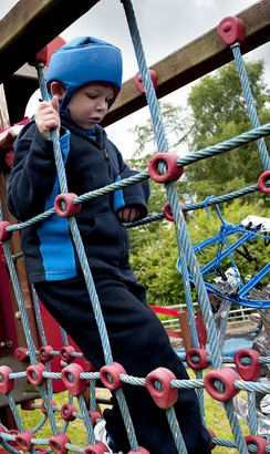 Young boy with protective headgear
                  traverses adventure playground