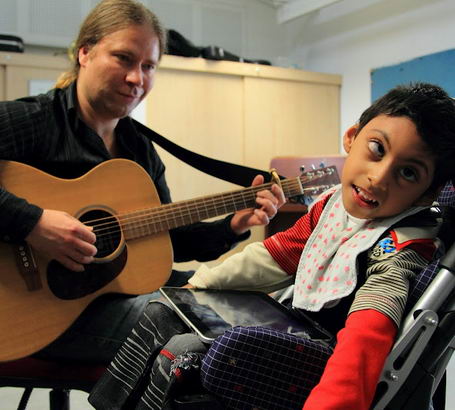 Young boy and teacher interact using guitar
                  and ipad