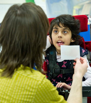 Adult showing a card to a girl in
                  a wheelchair