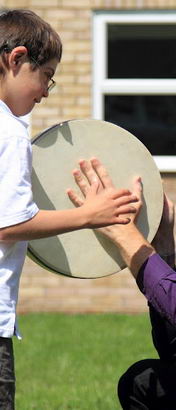A male teacher and a young boy use a drum
                  to interact in a school field
