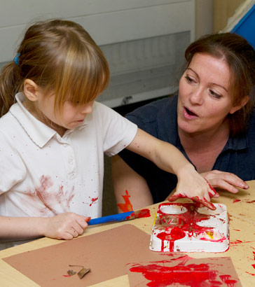 A young girl paints with her teacher