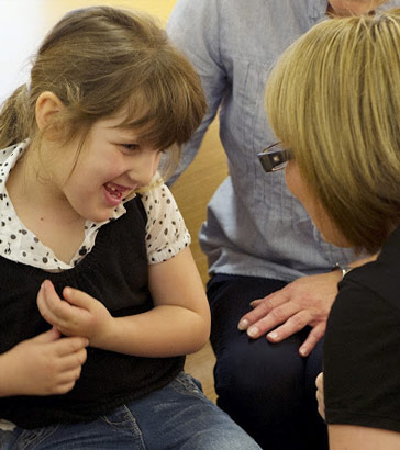 A girl smiles as a teacher talks
                  to her]]