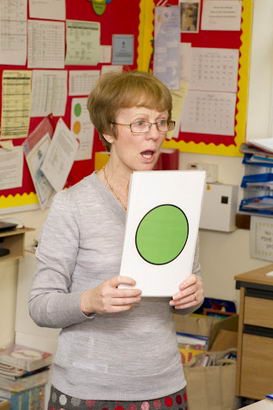 A teacher holds up a self-assessment
                  card depicting a green disc