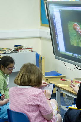 Three pupils and a teacher use
                  a large touch-screen