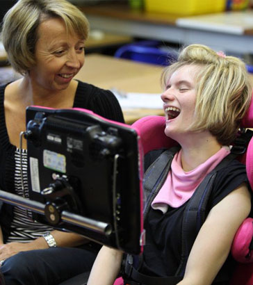 A teacher and two pupils with assistive
                  devices laugh and smile