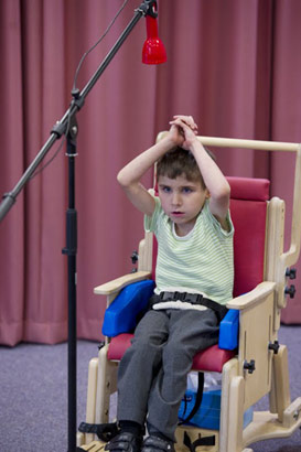 young boy in stripey top and supportive
                  chair uses aural equipment to communicate