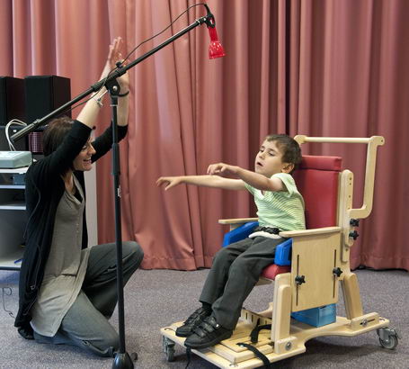 A teacher uses an assistive
                  device on a microphone stand to communicate with a young boy in a supportive chair