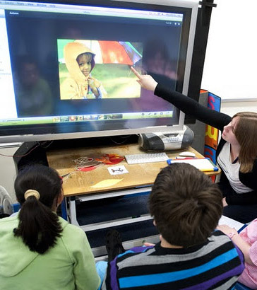 A teacher uses an interactive
                  board to engage with three of her pupils