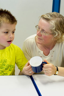 A teacher and a young boy use
                  a blue mug as an object of reference
