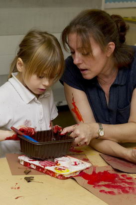 A young girl and teacher engage
                  through messy painting