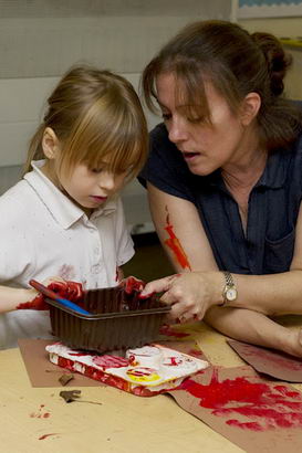 A young girl and teacher engage
                  through messy painting