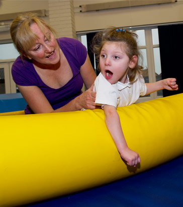 A young girl with her teacher on
                  a safety mat in a school gym