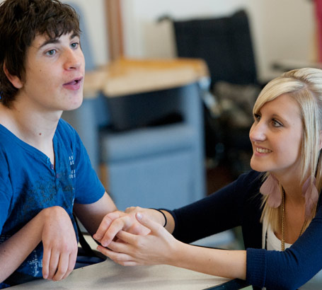 A young female teacher coaxes
                  a teenage boy to communicate