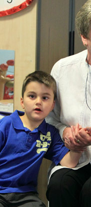 An older female teacher comforts, supports
                  and holds the hand of a young boy