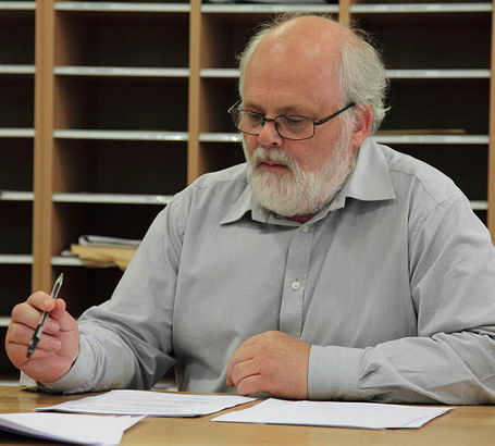 Gentleman with large grey beard sitting
                  at table carrying out an audit