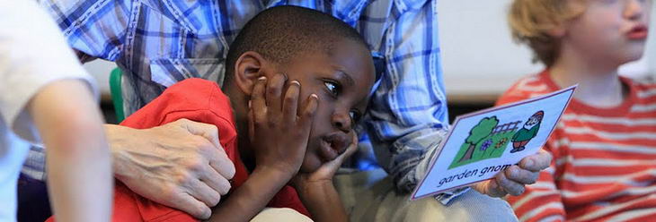 A young boy and his teacher interact using a garden gnome picture
