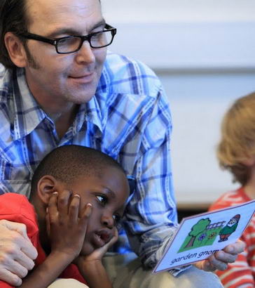A young boy and his teacher interact using a garden gnome picture