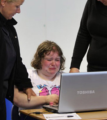 Two teachers comfort a distressed pupil
                  who is using a laptop
