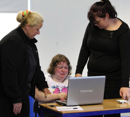 Two teachers comfort a distressed pupil
                  who is using a laptop