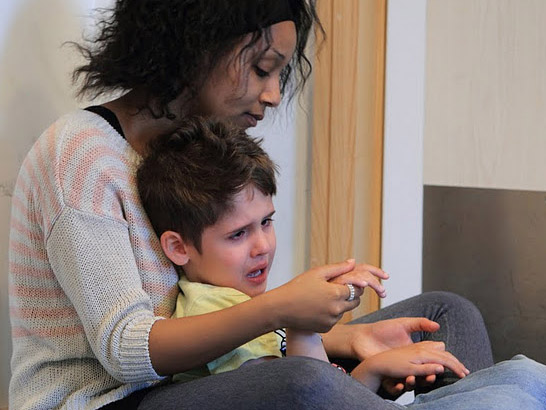 A teacher comforts a young boy who is distressed