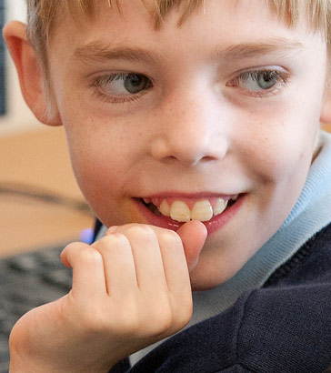 a young boy smiles at the camera
                  as he works on a computer