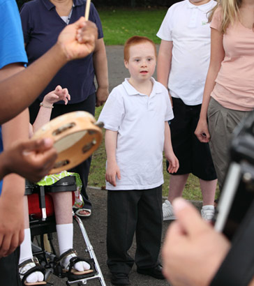 A young boy transfixed by music surrounded
                  by a support group of teachers and pupils
