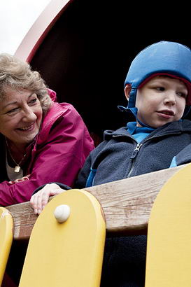 A female teacher and a young boy
                  with protective headgear have fun in the treehouse of an adventure playground