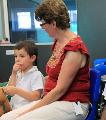 A male teacher smiles with one boy whilst
                  another boy lies on his lap